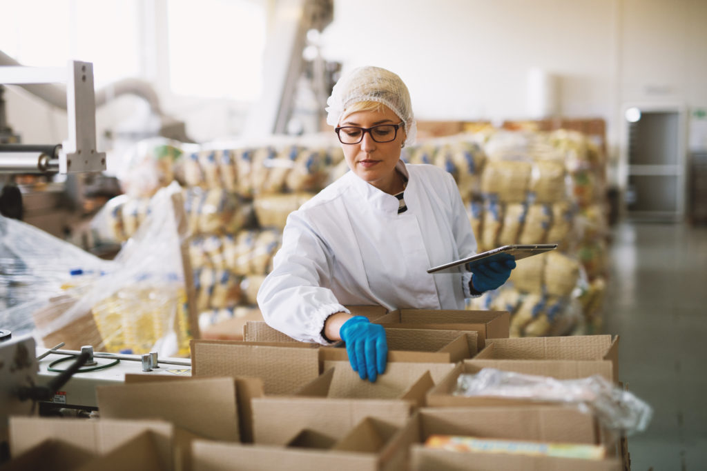 Young female employee in sterile clothes is checking packages ready to be delivered.