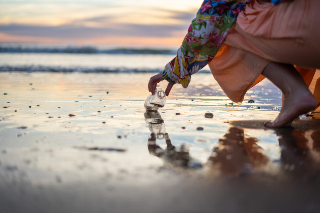 A woman cleaning a beach full of plastic bottles and rubbish in the sea