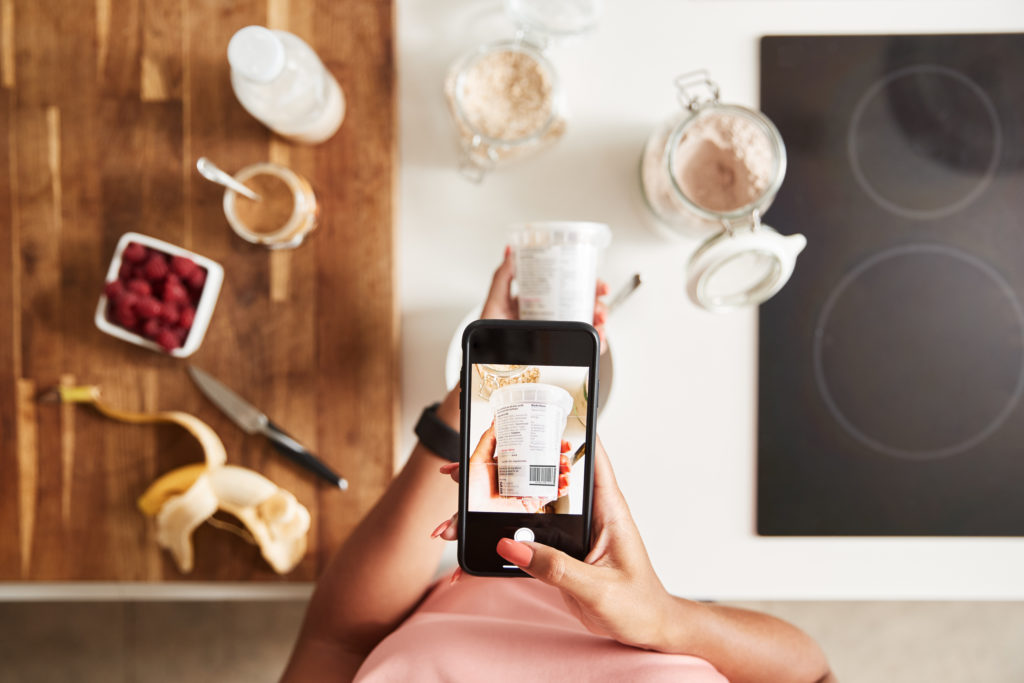 Woman Wearing Fitness Clothing Scanning QR Code On Food Packaging To Find Nutritional Information