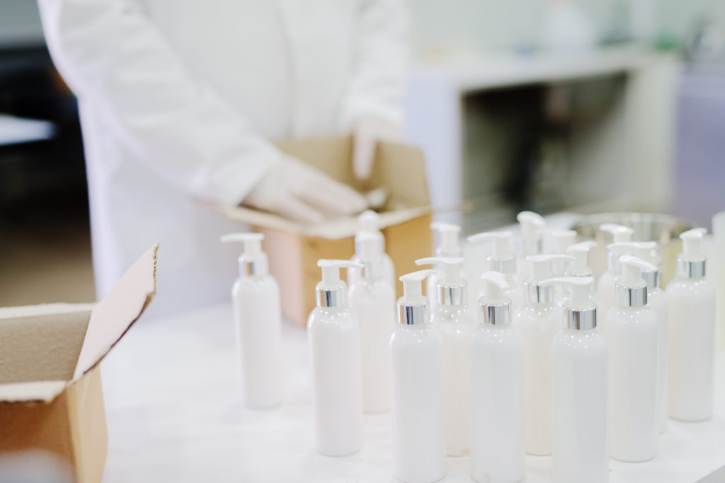 Close up of bottles with lotion. Males hands putting bottles in carton box in background.