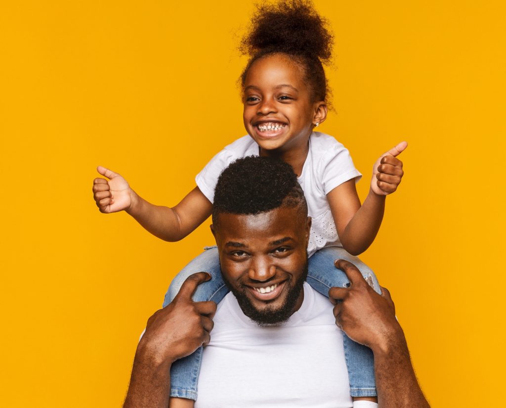 Adorable little african girl gesturing thumbs up on daddy's shoulders