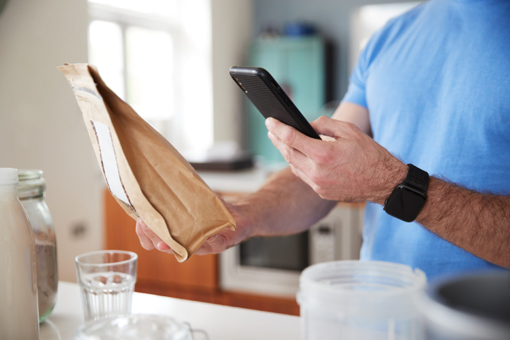 Man Wearing Fitness Clothing Scanning QR Code On Food Packaging To Find Nutritional Information