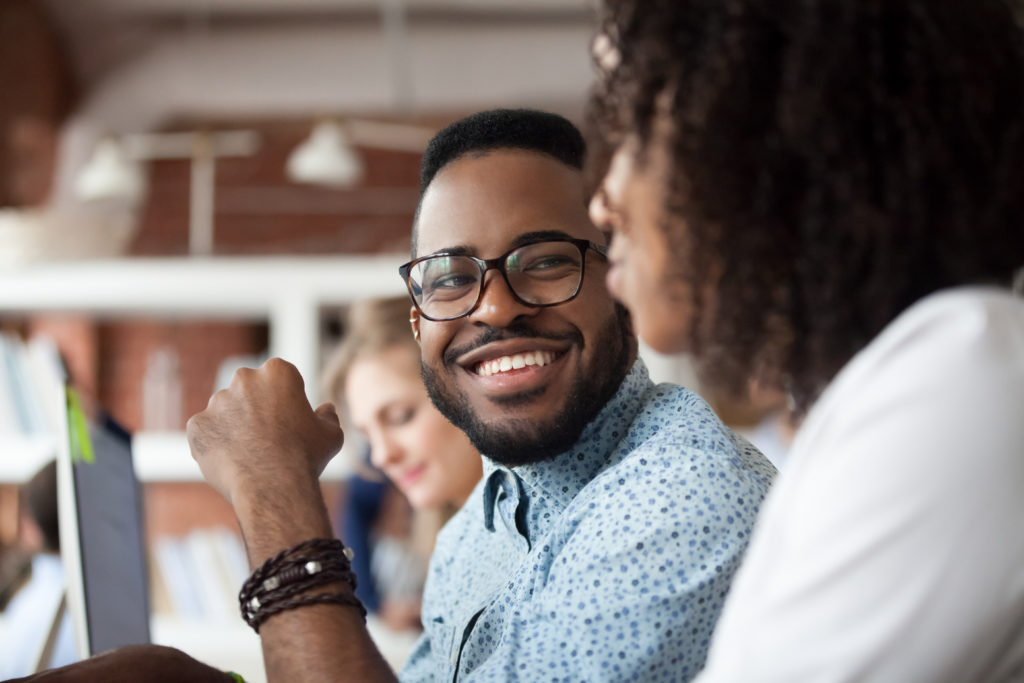 Smiling African American male employee look at colleague chattin