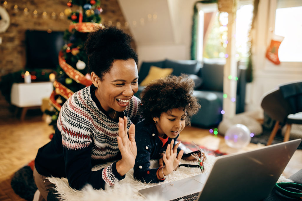 Cheerful black mother and daughter greeting someone during video call on Christmas.